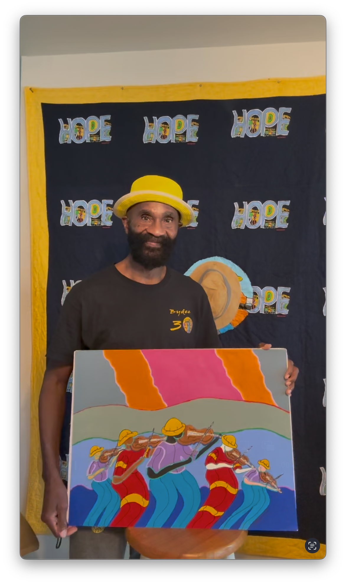 Brian "BYDEE man" Joseph holding a colorful painting in front of a 'HOPE' backdrop
